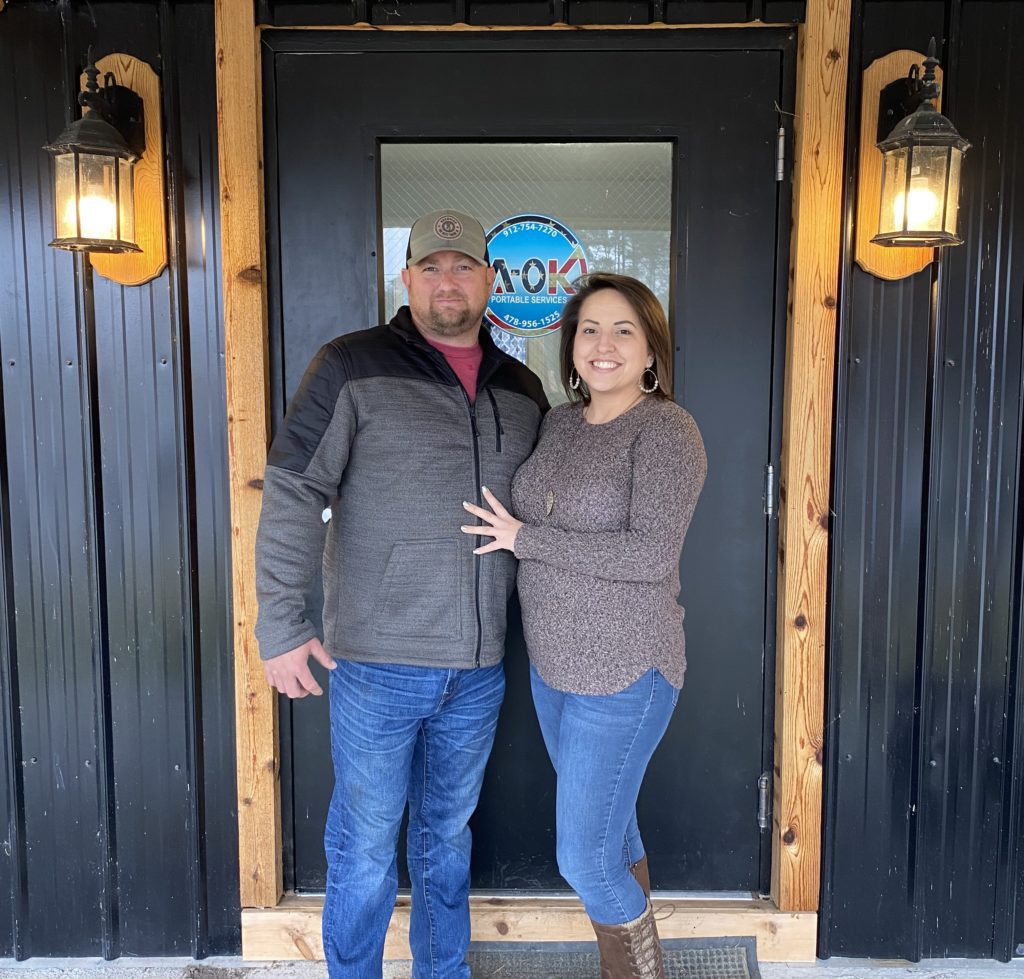 Owners in front of a door with a logo on it